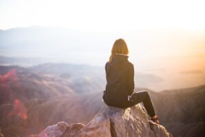 Frau sitzt auf einer Bergspitze und schaut in die Weite